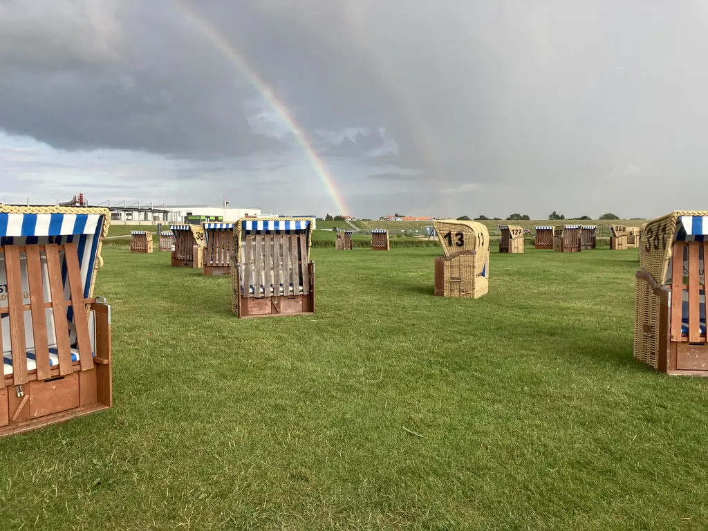 Strandkörbe auf der Wiese am Strand unter einem Regenbogen